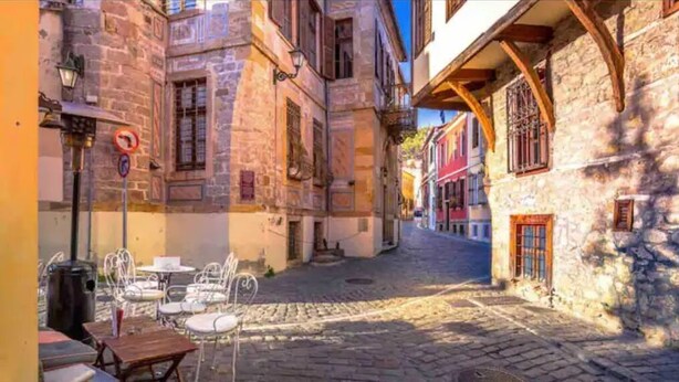 A cobblestone street with stone buildings, outdoor seating, and a no parking sign.