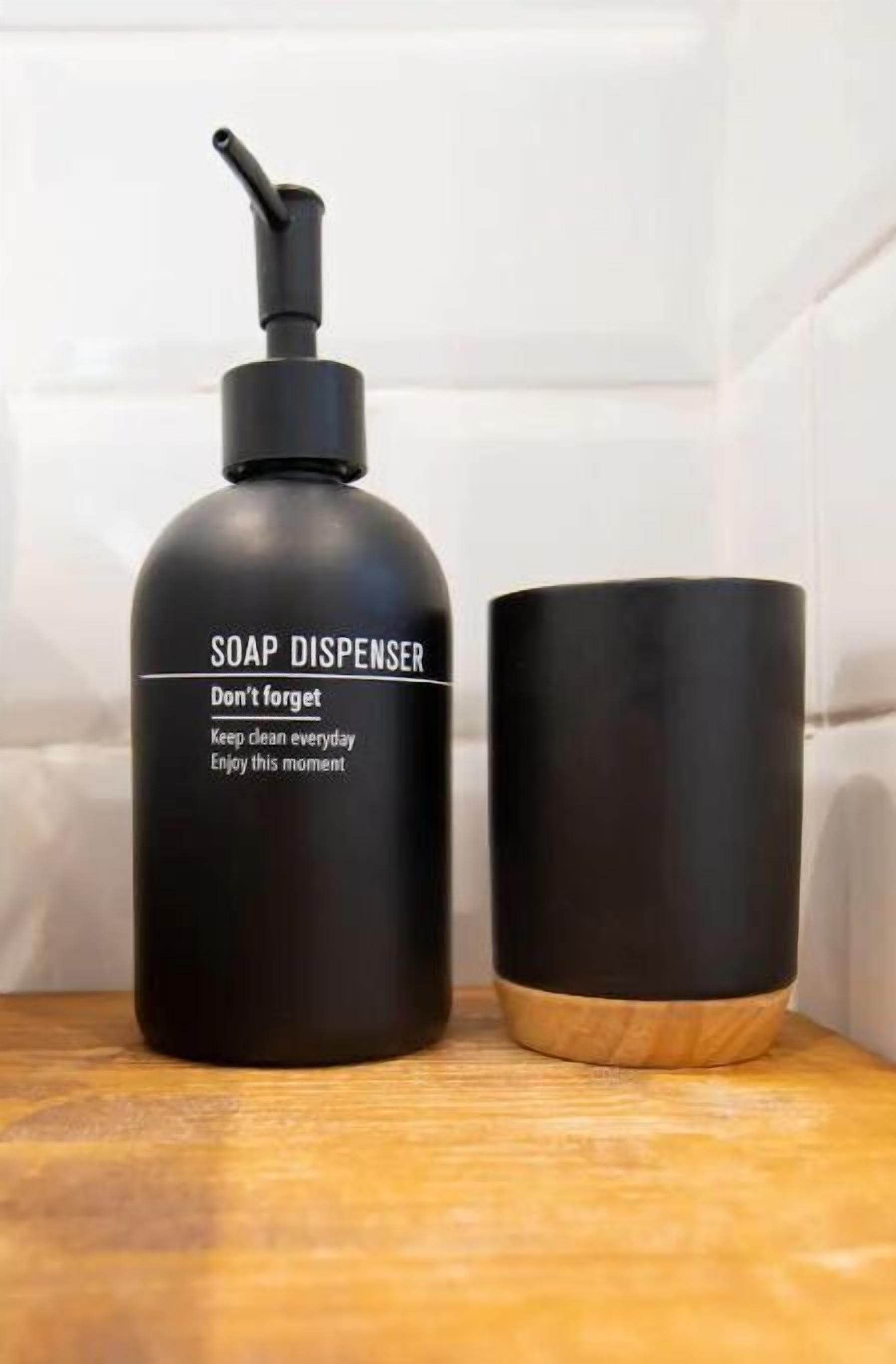 Un distributeur de savon noir avec un mécanisme de pompage, posé sur une surface en bois, à côté d’une tasse noire.