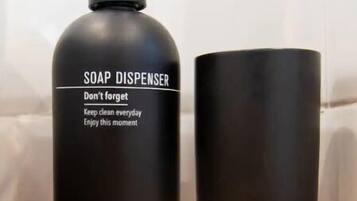 Un distributeur de savon noir avec un mécanisme de pompage, posé sur une surface en bois, à côté d’une tasse noire.