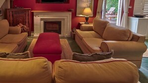A living room with a fireplace, two sofas, and a red ottoman. - Cook’s Cottage, Franschhoek village (Franschhoek)