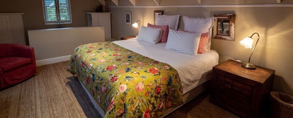 A bedroom with a bed, a nightstand, a red chair, and a window.