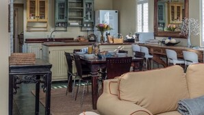 A cozy living room with a beige sofa, a dining area with a wooden table and chairs, and a kitchen with green cabinets and a white refrigerator. - Cook’s Cottage, Franschhoek village (Franschhoek)
