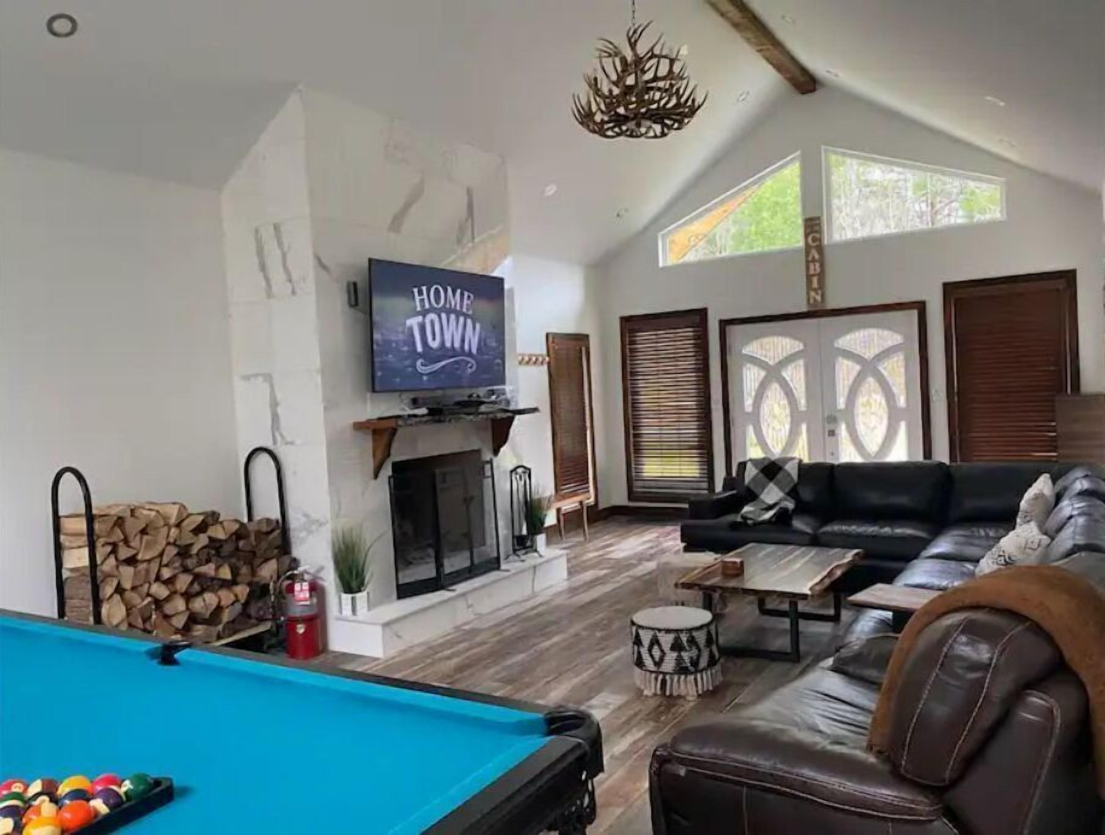 A living room with a pool table, a sofa, a fireplace, and a television displaying "HOME TOWN".