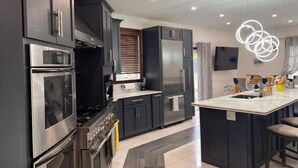 Una cocina moderna con armarios oscuros, electrodomésticos de acero inoxidable y una isla central con taburetes de bar.