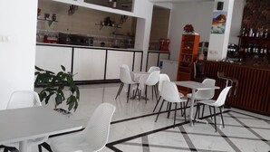A modern dining area with white chairs and tables, a kitchen in the background, and a bar area with bottles. - Danakil Hotel (Addis Ababa)