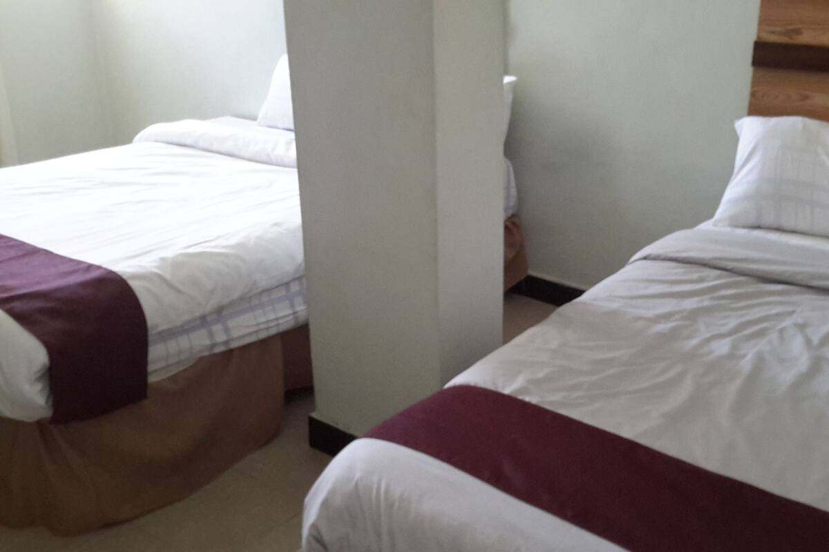 Two single beds with white and maroon bedding, a wooden headboard, and a white wall.