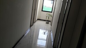 A corridor with a shiny tiled floor, a potted plant, and a window with a view of a green fence. - Danakil Hotel (Addis Ababa)