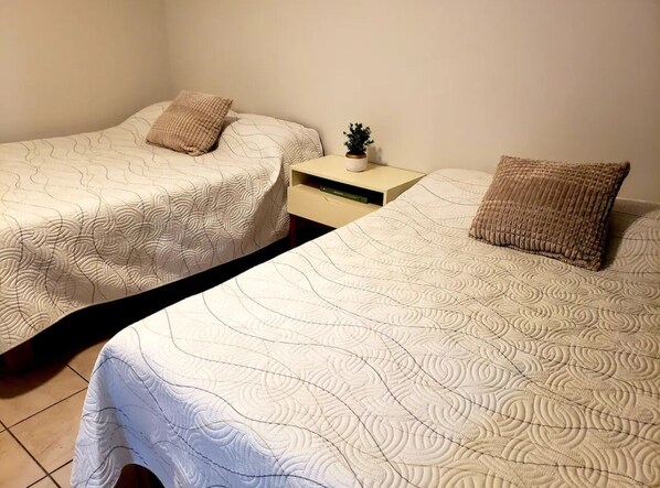 Two single beds with matching headboards and footboards, a bedside table with a small plant, and a nightstand with a lamp.