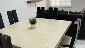 A modern dining area with a wooden table, black chairs, a potted plant, a mounted TV, and a window with blinds. - 3 Bedrooms Home 5 min Walking Distance to El Malecon (La Paz)