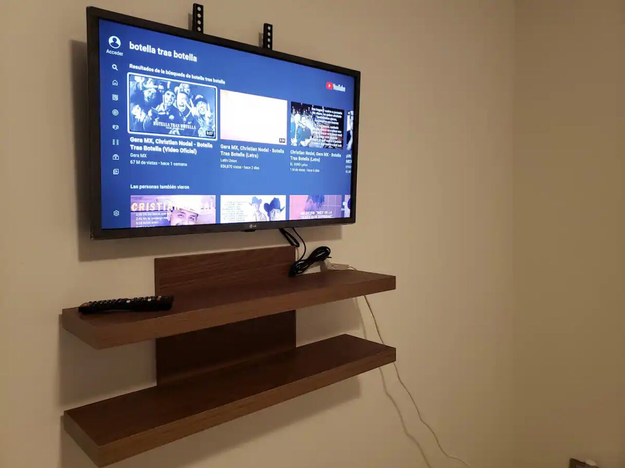 Una televisione a schermo piatto montata a parete, con uno scaffale in legno sottostante.