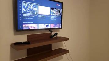 Una televisione a schermo piatto montata a parete, con uno scaffale in legno sottostante.