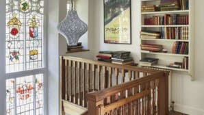 Un escalier avec des balustrades en bois, un vitrail, une lampe et une bibliothèque remplie de livres.