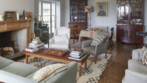 Un salon chaleureux avec une cheminée, une table basse avec des livres, un fauteuil blanc et un fauteuil gris.