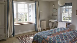Une chambre à coucher avec un lit, une fenêtre, un radiateur, un lavabo et un miroir.