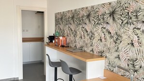 A modern kitchen with a wooden countertop, two black bar stools, a stainless steel sink, and a decorative wall with a tropical leaf pattern. - B&B HoMa (Naples)