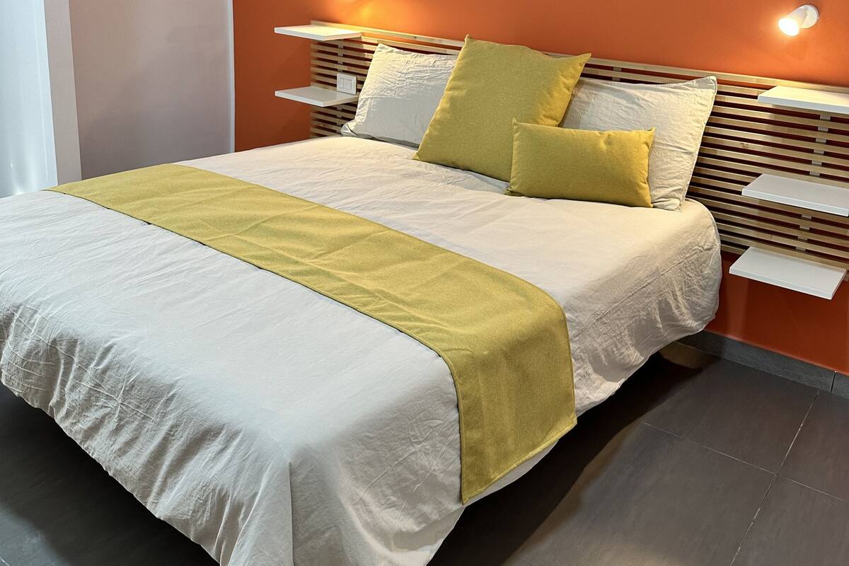 Una cama bien tendida con una colcha blanca y amarilla, dos almohadas y un cabecero de madera.
