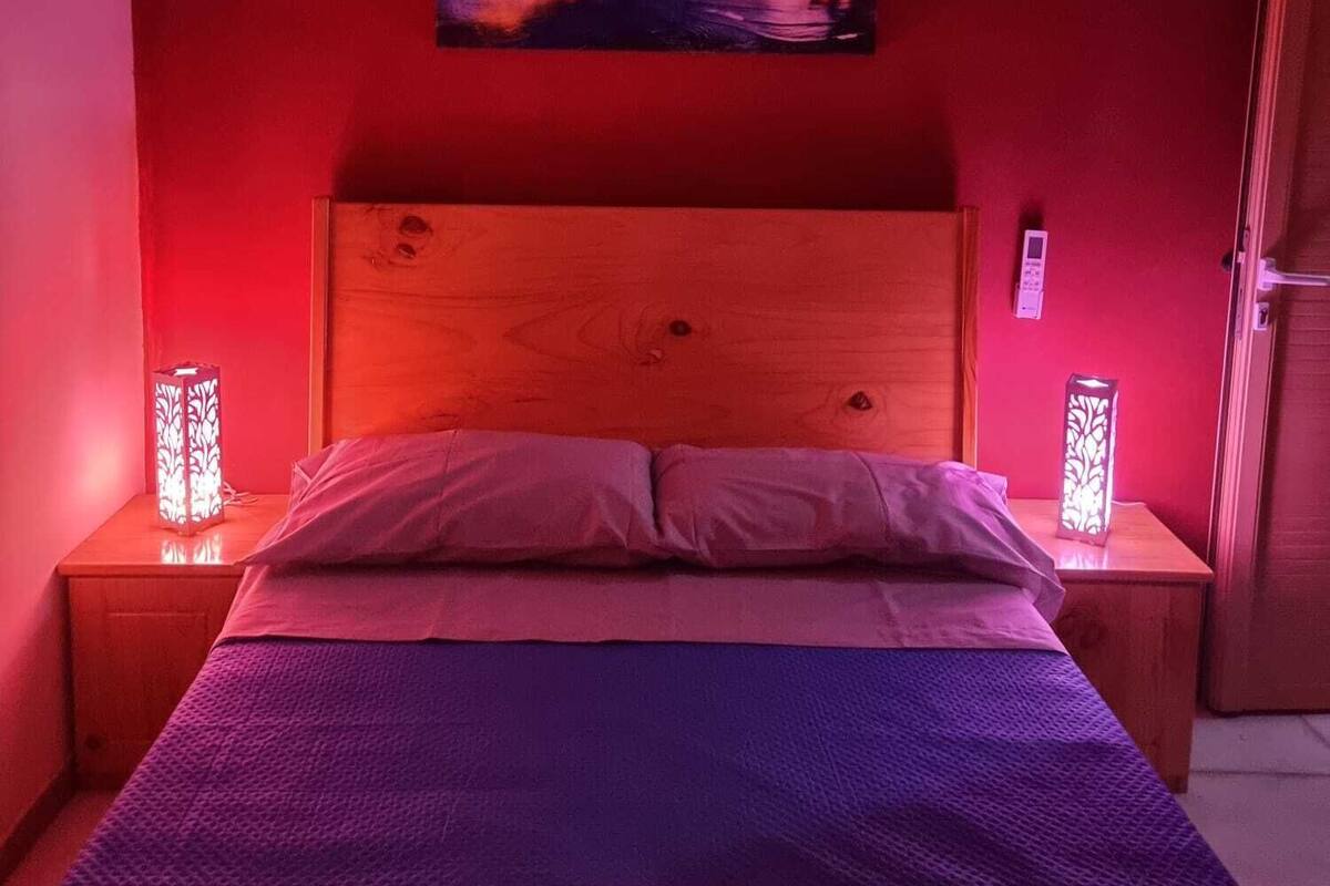 Ein Schlafzimmer mit einem Holzkopfteil, einem Bett mit lila Decke und zwei Nachttischen mit dekorativen Lampen.