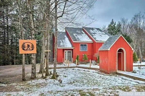 Een rode woning met een klein bijgebouw, omringd door bomen en een besneeuwde grond.