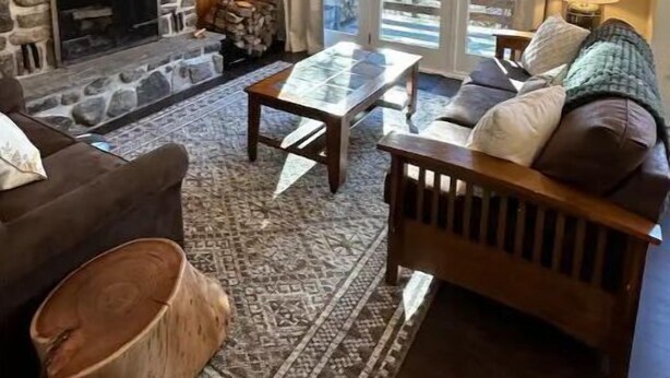 Una sala de estar acogedora con una chimenea de piedra, un televisor montado en la pared, una mesa de centro de vidrio y un sofá con cojines.