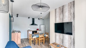 A compact living space with a dining area, kitchenette, and a TV mounted on a wooden wall. - Gîte du Thouet - Appt avec piscine partagée (Montreuil-Bellay)