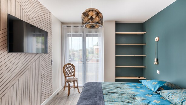 A modern bedroom with a large bed, a mounted TV, and built-in shelves. - Gîte du Thouet - Appt avec piscine partagée (Montreuil-Bellay)