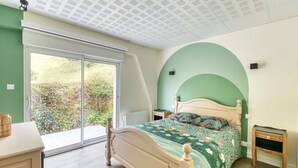 Ein Schlafzimmer mit einem Bett, einem Nachttisch, einer Kommode und einem großen Fenster.
