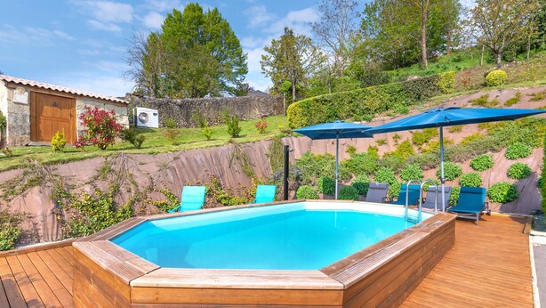 Eine Holzterrasse mit Schwimmbecken, umgeben von viel Grün und einer Steinmauer.