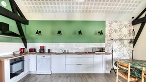Eine moderne Küche mit weißen Schränken, einer grünen Spritzschutzwand und einem Esstisch aus Holz mit Stühlen.