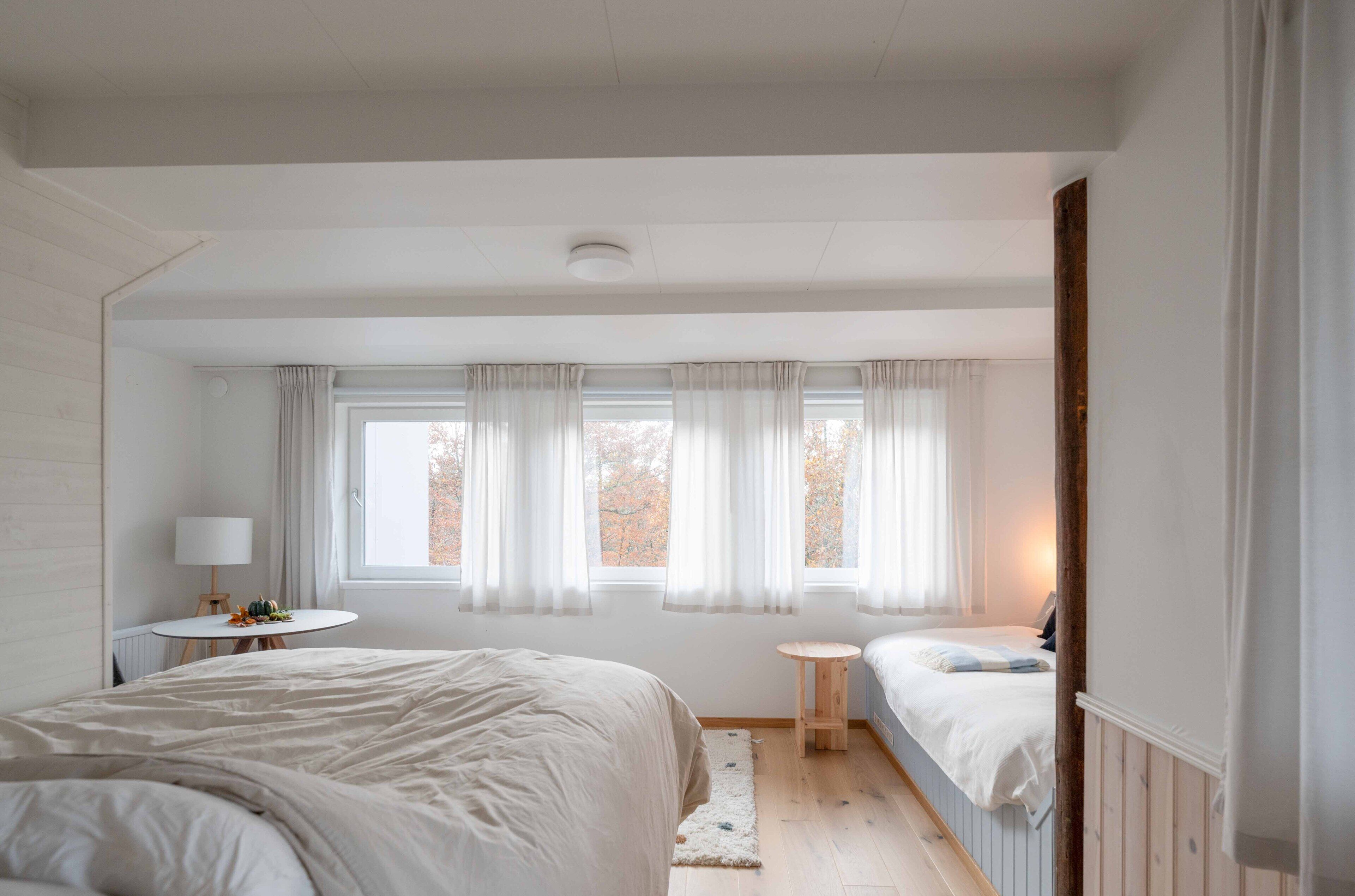 Un dormitorio con dos camas, una mesa redonda y un ventanal con cortinas.