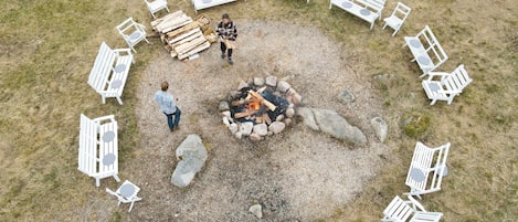 A circular arrangement of white benches around a central fire pit with logs.