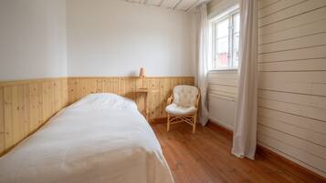A room with a single bed, a chair, a window with curtains, and wooden walls.