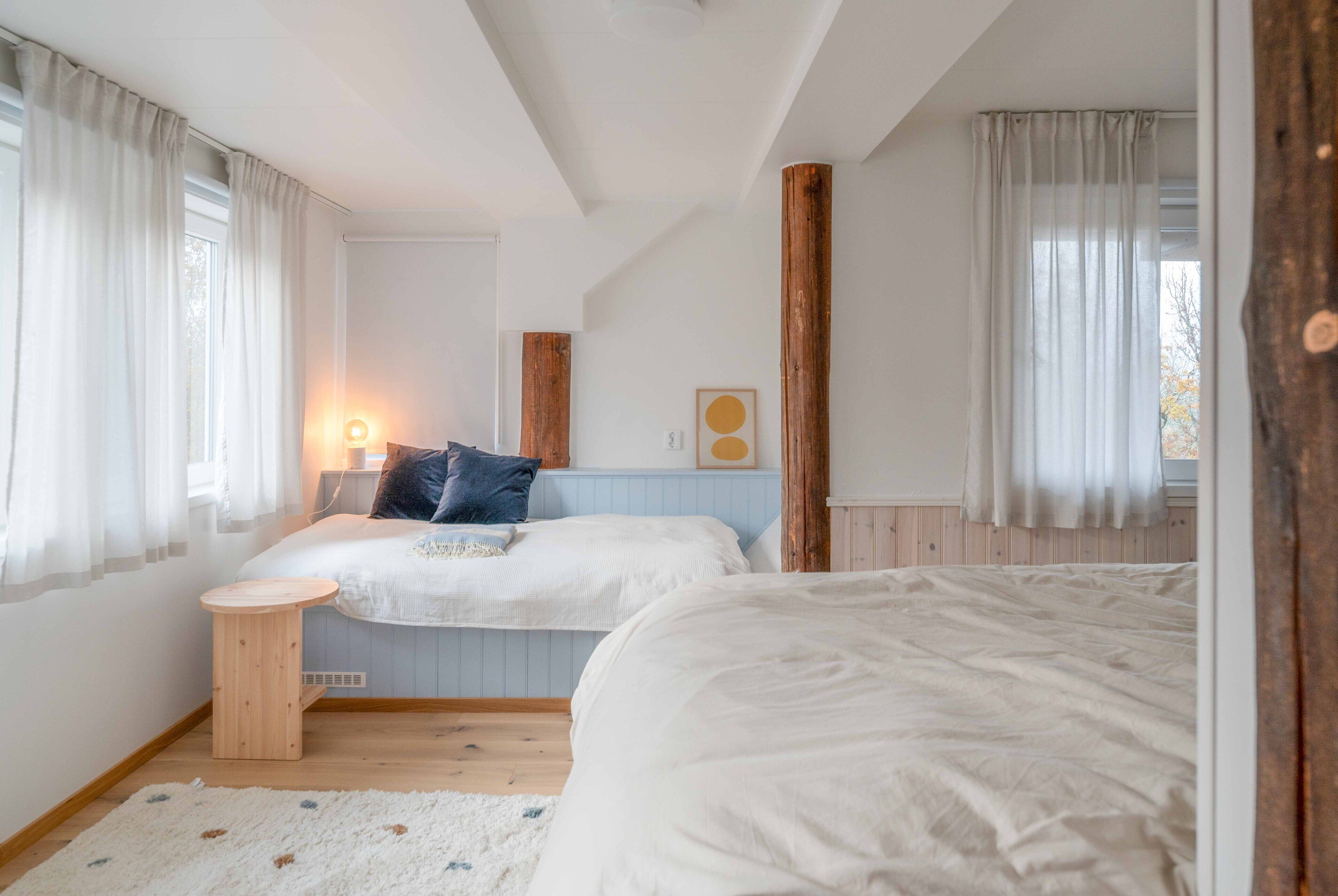 Een slaapkamer met twee bedden, een klein houten krukje en een nachtkastje met een lamp.