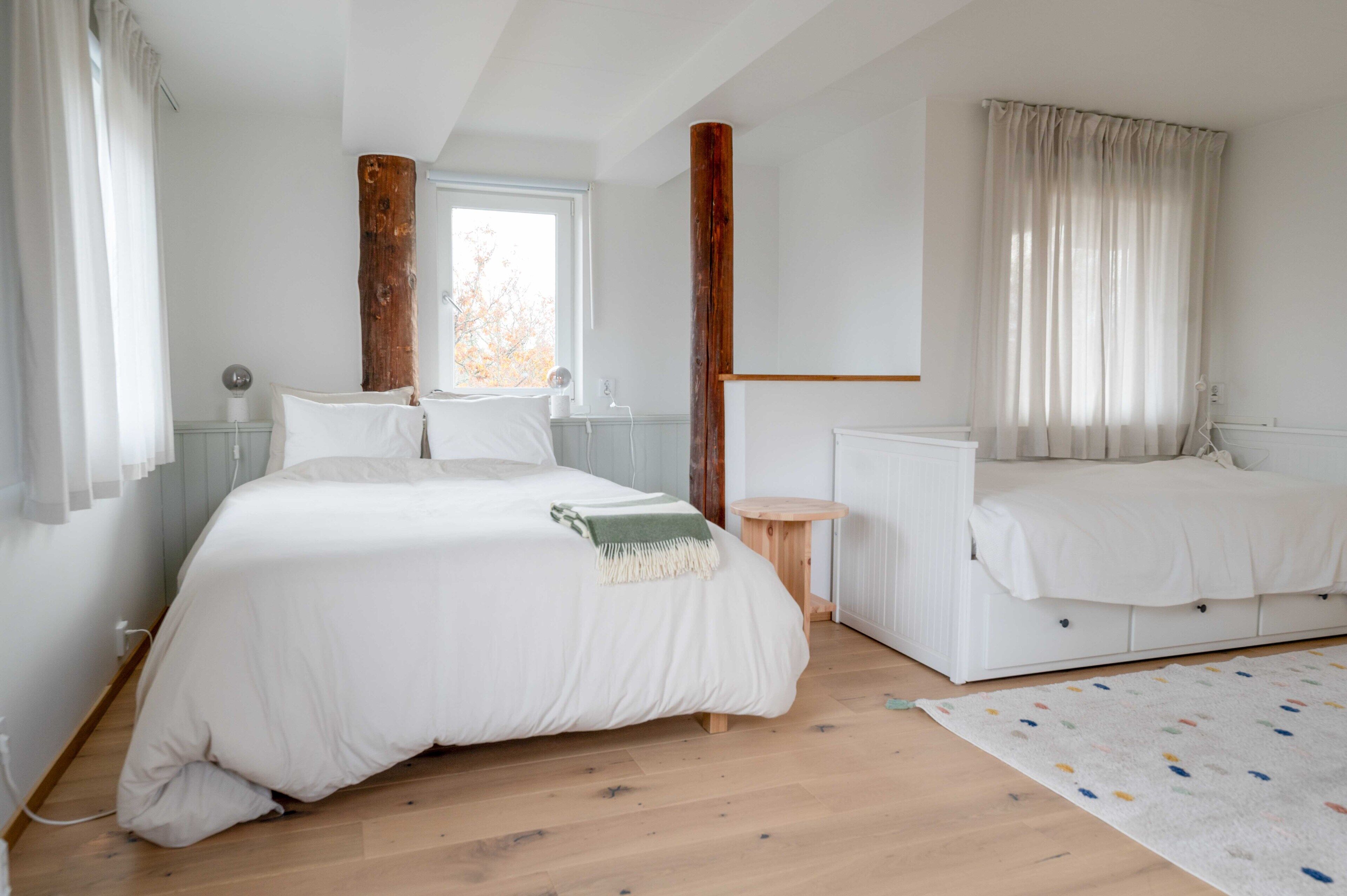 A bedroom with a large bed, a smaller bed, a wooden floor, and a window with curtains.