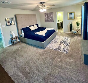 Quarto com cama grande, ventilador de teto e vista para o banheiro adjacente.