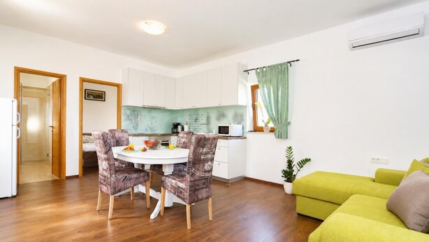 En moderne stue med et spiseområde, en grøn sofa og et køkken med hvide skabe.