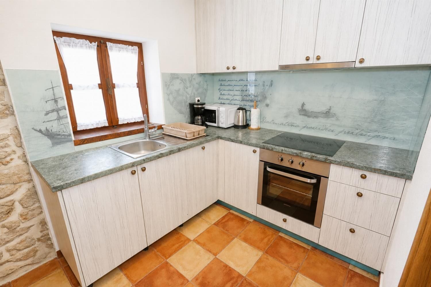 A kitchen with a sink, a stove, and a window with curtains.