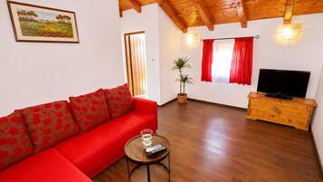 A living room with a red sofa, a wooden TV stand, a potted plant, and a painting on the wall.