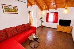 Ein Wohnzimmer mit einem roten Sofa, einem Holz-Fernsehschrank, einem Blumentopf und einem Bild an der Wand.