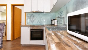Et kompakt køkken med indbygget ovn, mikroovn og en backsplash med et motiv af drueblade.
