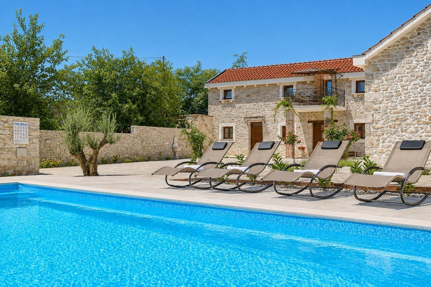 A poolside area with lounge chairs and a stone building with a tiled roof.