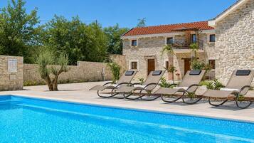 A poolside area with lounge chairs and a stone building with a tiled roof.