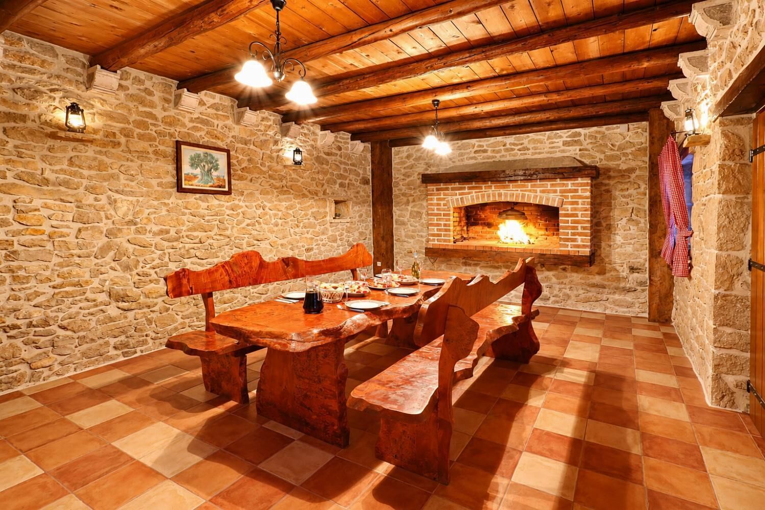 A rustic dining area with a stone wall, wooden ceiling, and a brick fireplace.