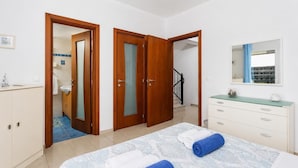 Un dormitorio con cama, cómoda, espejo y baño visible a través de una puerta abierta.