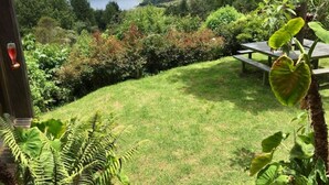 A lush garden with a view of a lake and hills, a wooden bench, and a door with a red handle. - Embalse del Sisga- El Cobijo Casa de Campo (Cundinamarca)