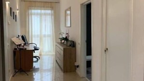 Un hall d’entrée spacieux, avec un bureau et une chaise, un petit meuble et une porte donnant sur une autre pièce.