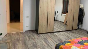 Une chambre avec une grande armoire, un lit recouvert d’une courtepointe aux couleurs vives et un plancher en bois.