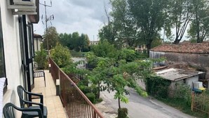 Un balcon donnant sur une rue résidentielle, avec un petit arbre et une clôture.