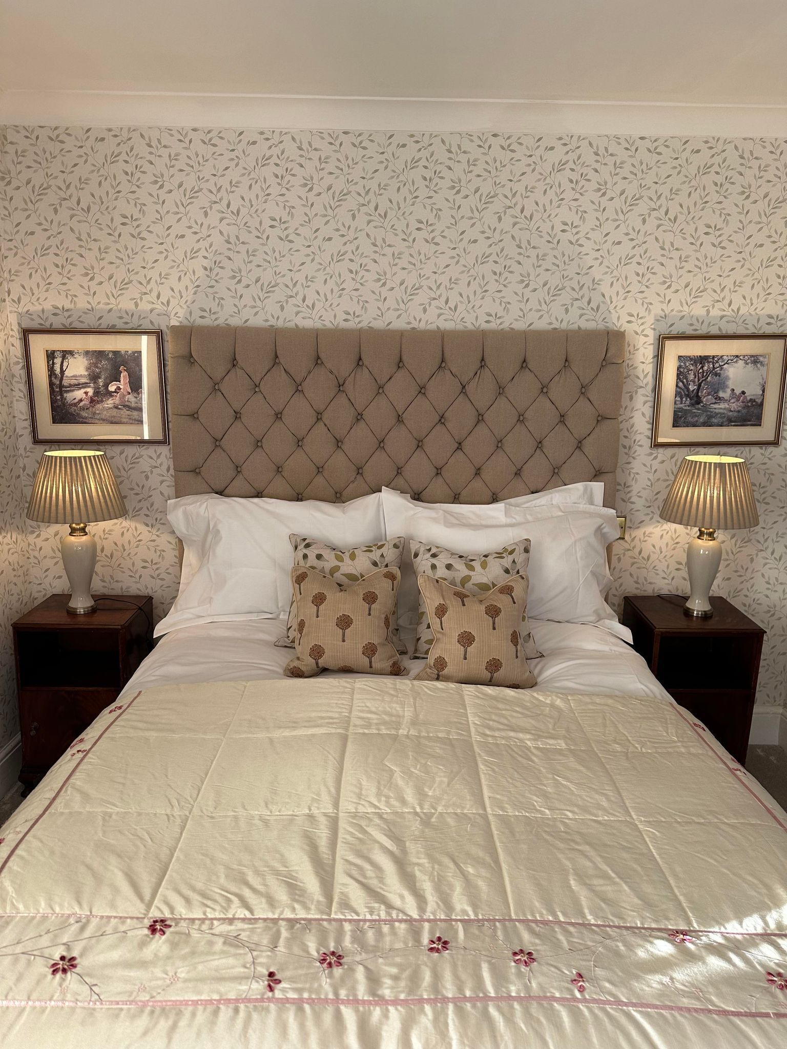 A neatly made bed with a tufted headboard, two bedside tables with lamps, and floral wallpaper.