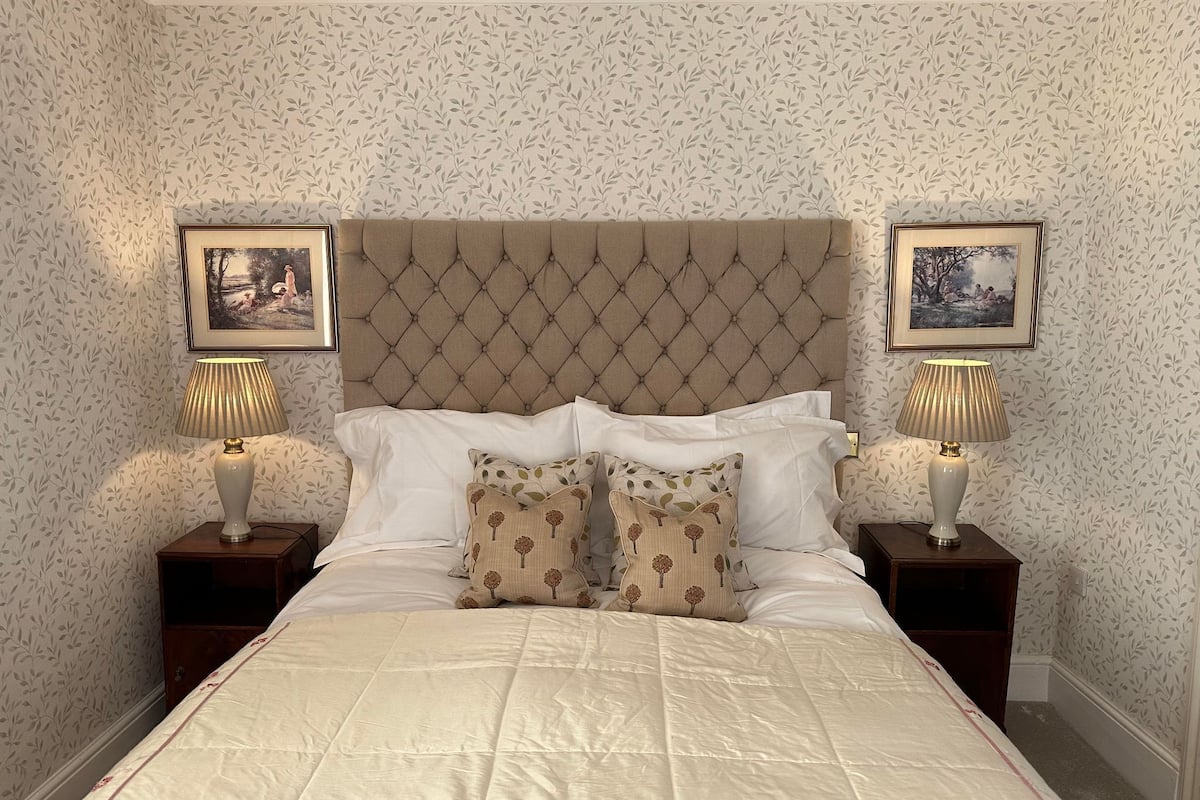 Une chambre à coucher avec une tête de lit capitonnée, du linge de lit blanc et deux lampes de chevet.