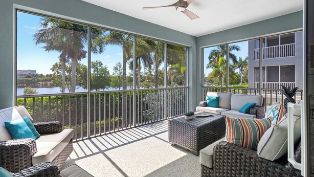 A balcony with wicker furniture, a ceiling fan, and a view of palm trees and water. - Otter Lagoon at One Particular Harbour  379-103 Lagoon Views · Gaming · 3BR (Bradenton)